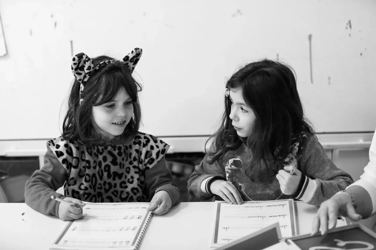 2 élèves discutant à leur bureau tout en accomplissent leur exercice écriture dans la bonne humeur et le partage ces sa l'apprentissage cher à l'école Galilée de saint Maximin - une école pour chacun